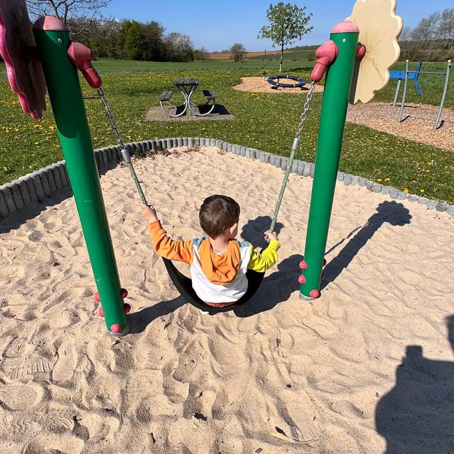 Kind schaukelt auf dem Spielplatz, von hinten gesehen