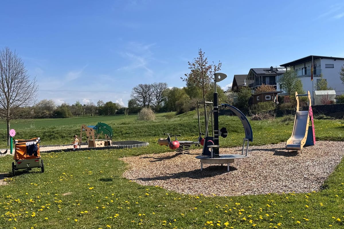 Spielplatz mit Rutsche, Karussell und Wiese an einem sonnigen Tag